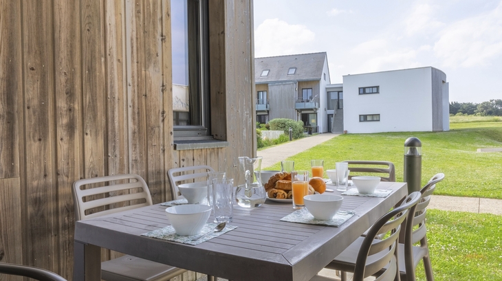 Terrasse mit gedecktem Tisch, Gebäuden und grüner Wiese im Hintergrund.