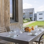 Terrasse mit gedecktem Tisch, Gebäuden und grüner Wiese im Hintergrund.