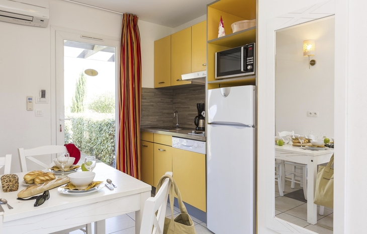 Kleine moderne Küche mit Esstisch, gelben Schränken und Fensterblick.