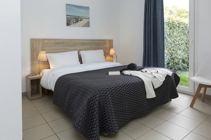 Schlafzimmer mit Doppelbett, zwei Nachttischen und großer Fensterfront.