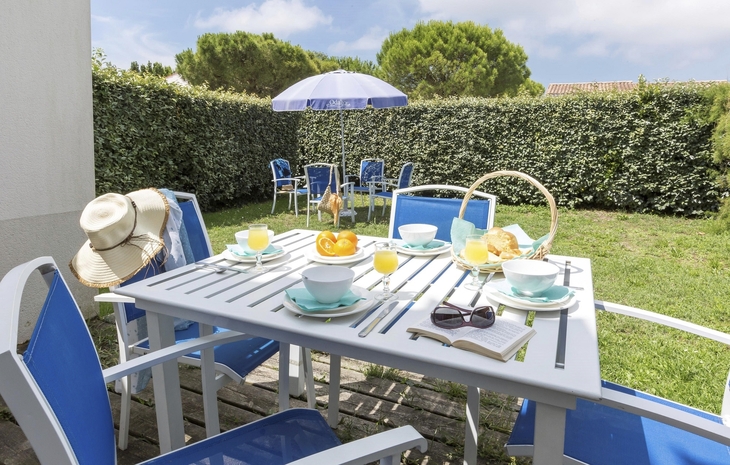 Garten mit Tisch, Stühlen, Sonnenschirm und Frühstücksgedeck im Freien.