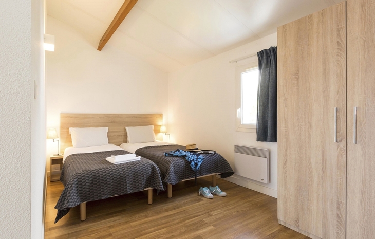 Zweibettzimmer mit Holzfußboden und Schrank in heller Ferienwohnung.