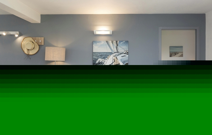 Wohnzimmer mit blauer Couch, Lampe, maritimem Bild und offenem Zugang zum Schlafzimmer.