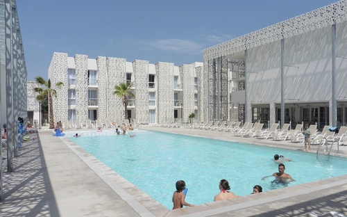Außenansicht eines modernen Hotels mit Pool und Sonnenliegen.