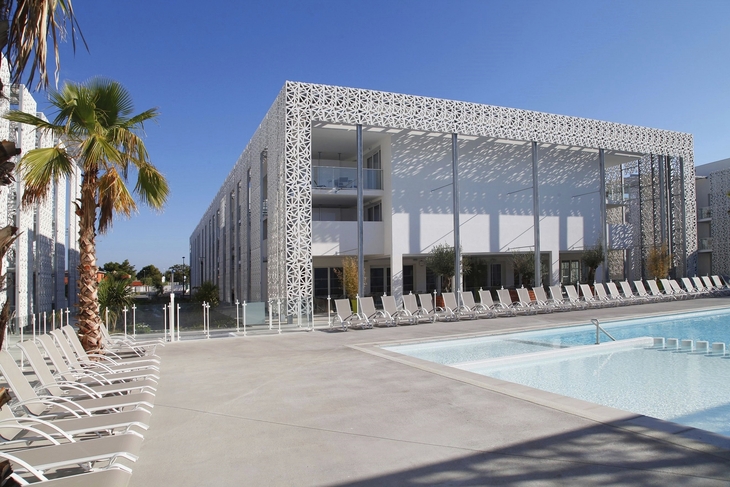 Modernes Gebäude mit Pool und Liegestühlen unter blauem Himmel.
