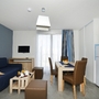 Wohnzimmer mit Esstisch, blauer Couch und Fernseher in moderner Ferienwohnung.