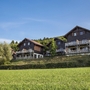 Drei Holzchalets auf einer grünen Wiese unter blauem Himmel.