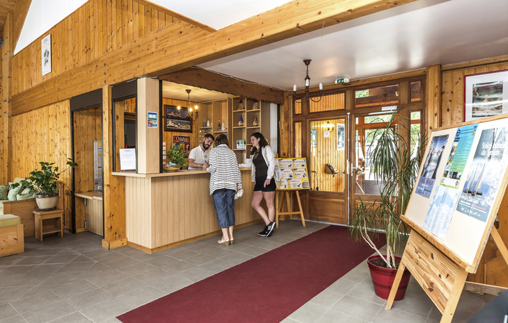 Rezeption in einer Holzlobby mit Gästen und Informationsmaterial.
