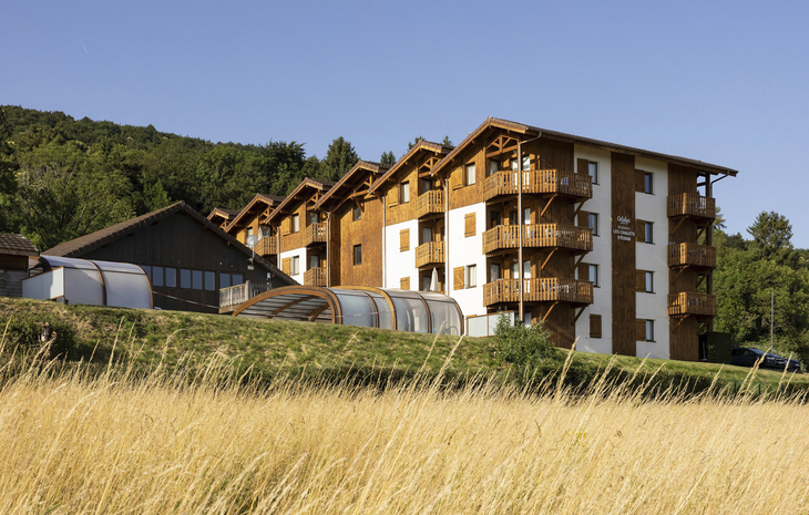 Appartementgebäude mit Balkonen in hügeliger, bewaldeter Landschaft.