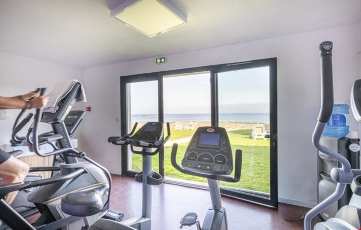 Fitnessraum mit Cardio-Geräten und Blick aufs Meer durch große Fenster.