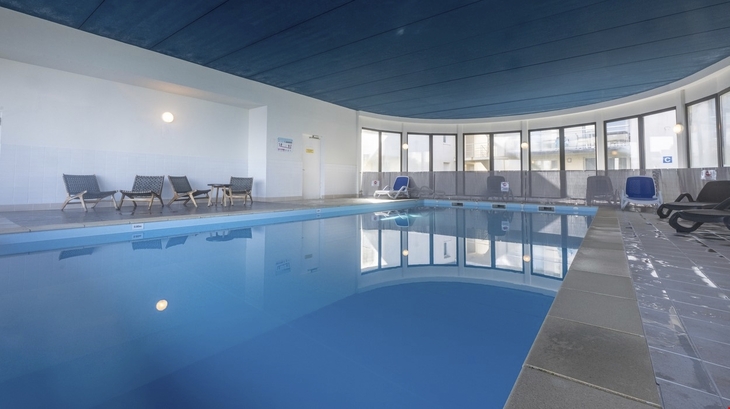 Innenpool mit blauen Liegestühlen und großem Panoramafenster.