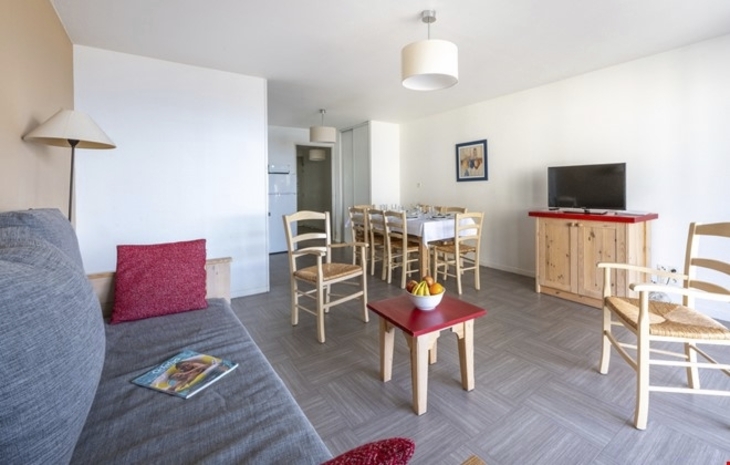 Helles Wohnzimmer mit Sofa, Esstisch, Stühlen und Fernseher.