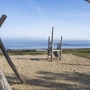 Kinderspielplatz mit Holzgeräten am Strand, Meer im Hintergrund.