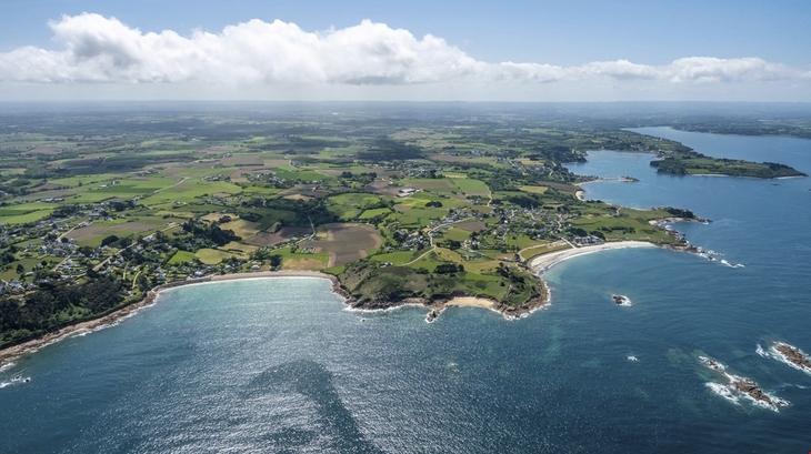 Luftaufnahme einer Küstenlandschaft mit grünen Feldern und blauem Meer.