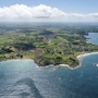 Luftaufnahme einer Küstenlandschaft mit grünen Feldern und blauem Meer.