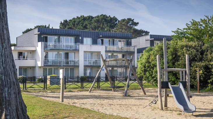 Apartmentgebäude mit Balkonen und einem Spielplatz im Vordergrund.