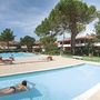 Außenansicht einer Ferienanlage mit Pool, Sonne und grünen Bäumen in Bibione.