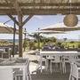 Terrasse mit Tischen, Stühlen, Sonnenschirmen und Blick auf das Meer.