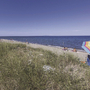 Strand mit Sonnenschirm und Gräsern, Meer im Hintergrund, klare blaue Himmel.