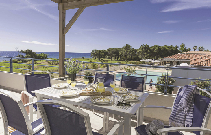 Terrasse mit Tisch, Stühlen, gedeckt für Frühstück, Meerblick, blauem Himmel.