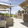 Terrasse mit Sitzgelegenheiten und Sonnenschirmen neben einer Holzbar bei sonnigem Wetter.