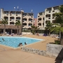 Außenansicht mit Pool, Palmen und mehrstöckigem Wohngebäude im Hintergrund.