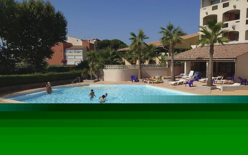 Menschen schwimmen im Außenpool, umgeben von Palmen und Gebäuden.