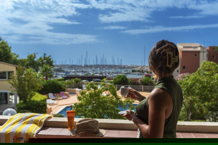 Frau auf Balkon mit Blick auf Hafen, bei sonnigem Wetter, Cap d'Agde.