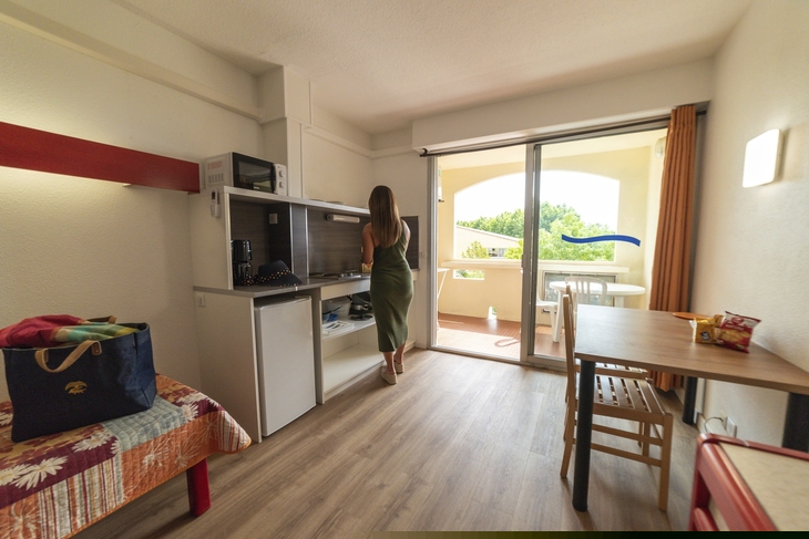 Frau in Studio-Apartment mit Balkon und Küchenzeile.