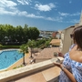 Frau auf Balkon mit Blick auf Pool und Hafen bei sonnigem Wetter.