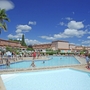 Poollandschaft in Ferienanlage mit Palmen und vielen Menschen unter blauem Himmel.