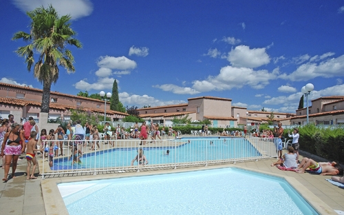 Poollandschaft in Ferienanlage mit Palmen und vielen Menschen unter blauem Himmel.