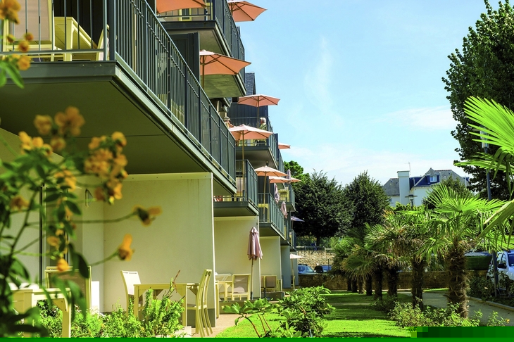 Balkone eines Hotels mit Sonnenschirmen, umgeben von Gartenanlagen und Palmen.