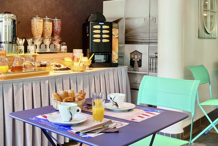 Frühstückstisch mit Croissants, Orangensaft und Kaffeemaschine im hellen Raum.