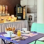 Frühstückstisch mit Croissants, Orangensaft und Kaffeemaschine im hellen Raum.