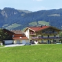 Haus in bergiger Landschaft mit blühenden Balkonen und Wiese im Vordergrund.