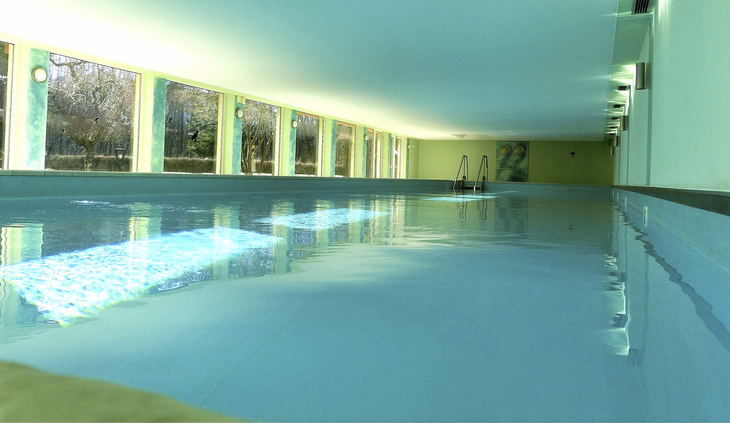 Innenpool mit großen Fenstern und hellgrünen Wänden in einer Appartementanlage.