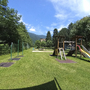 Spielplatz mit Rutsche und Klettergerüst in grüner Umgebung an einem sonnigen Tag.