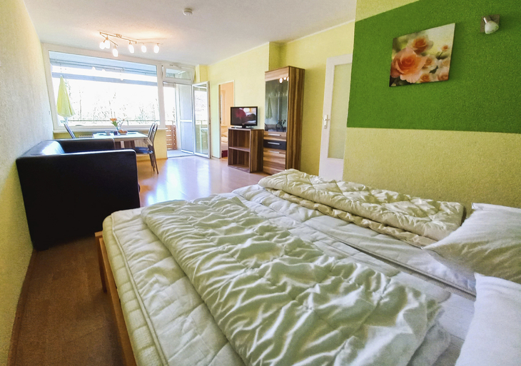 Schlafzimmer mit Doppelbett, Sofa, Esstisch, Fernseher und großem Fenster in Appartement.