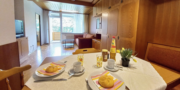 Wohnzimmer mit Esstisch, Brötchen, Getränke, Sofa und Zugang zum Balkon.