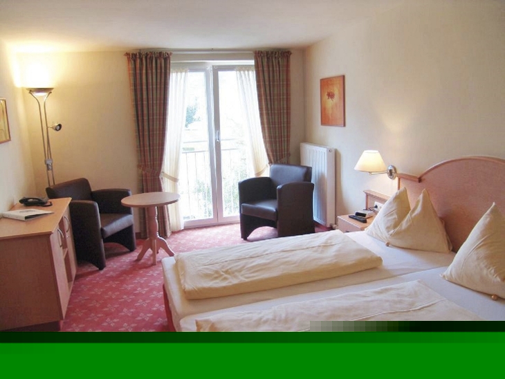 Hotelzimmer mit zwei Betten, Tisch, Stühlen und hellen Vorhängen.