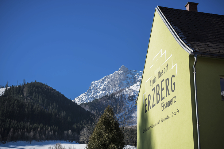 Gelbes Gebäude vor schneebedecktem Berg und blauem Himmel.