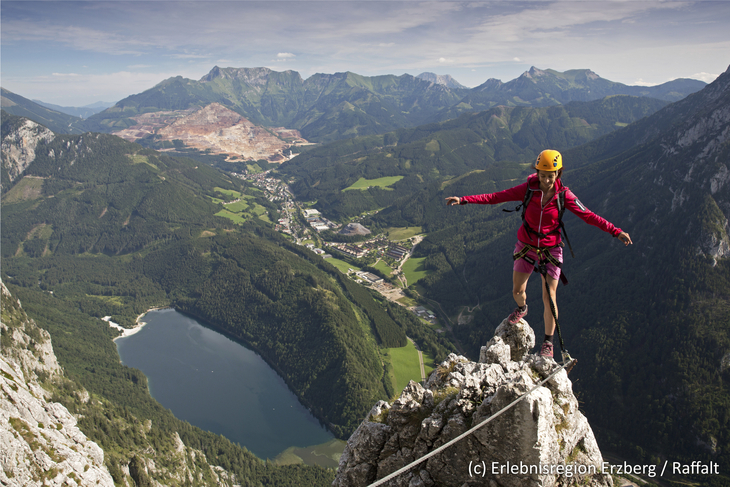 Kletterer auf Felsen mit Blick auf den Erzberg, See und Berge im Hintergrund.