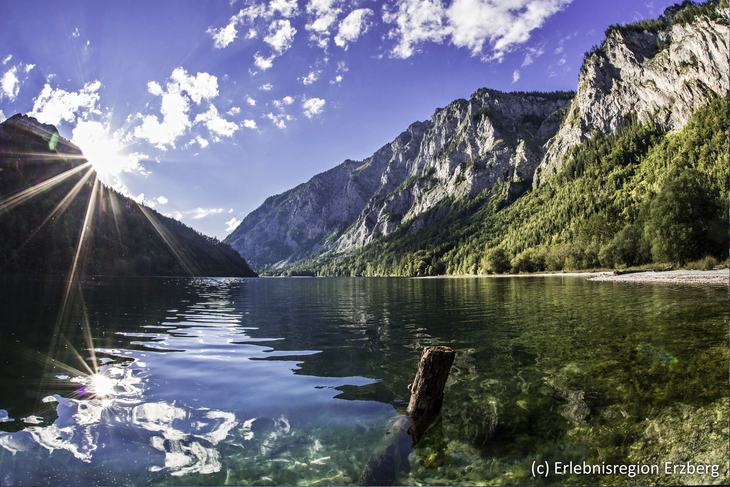 Bergsee mit umliegenden Bergen und strahlendem Sonnenschein.
