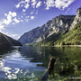 Bergsee mit umliegenden Bergen und strahlendem Sonnenschein.