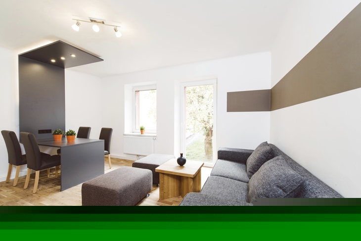 Moderner Wohnbereich mit grauem Sofa und Esstisch im Hintergrund.