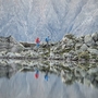 Zwei Wanderer auf einem Felsweg bei einem Bergsee, Berge im Hintergrund.
