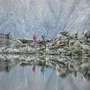 Zwei Wanderer auf einem Felsweg bei einem Bergsee, Berge im Hintergrund.