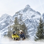 Zwei Personen rodeln im Schnee vor verschneitem Bergpanorama in Tirol.