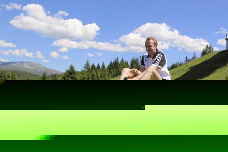 Person auf Sommerrodelbahn in grüner Alpenlandschaft mit blauem Himmel.